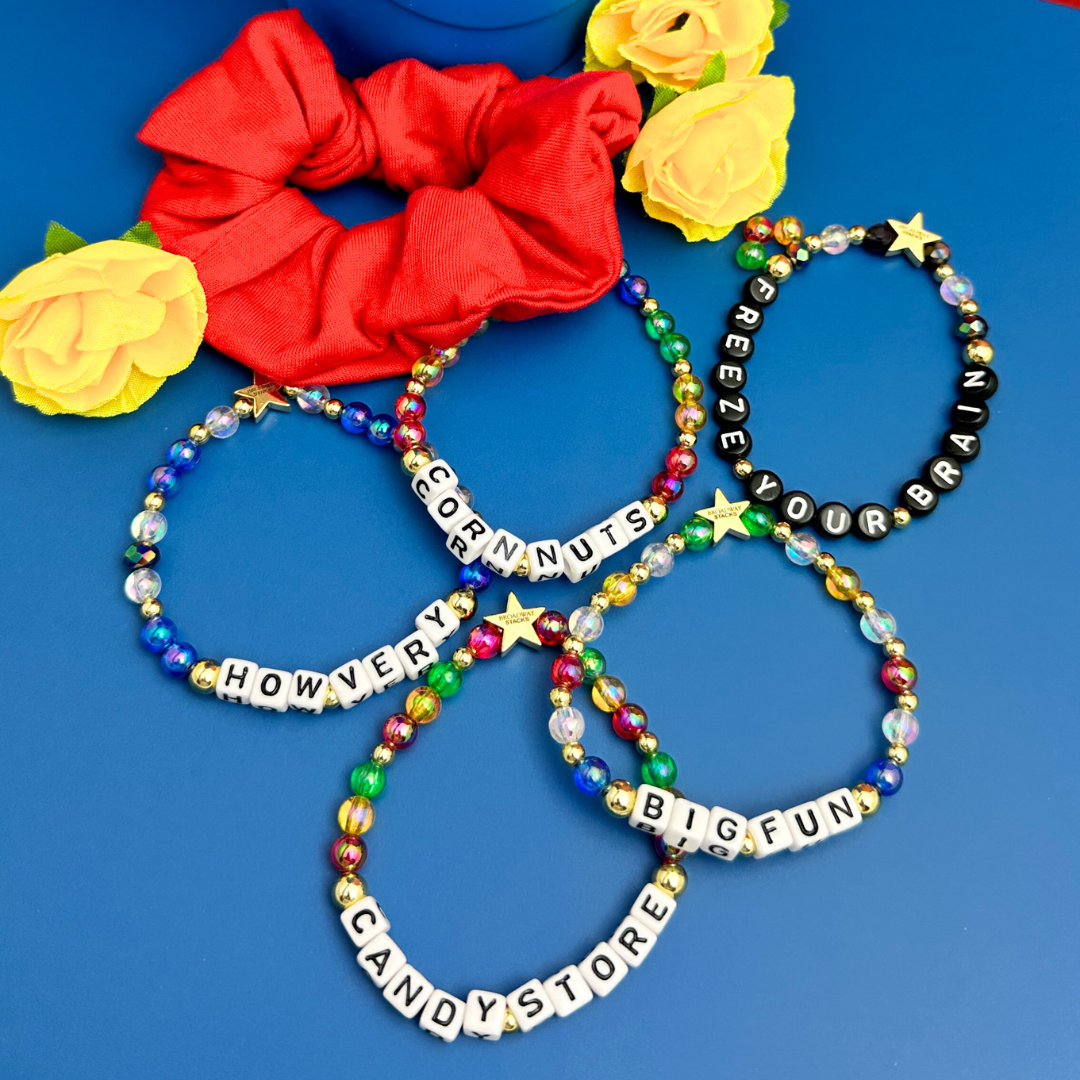 Broadway Stacks CORN NUTS Collection. 5 stretch bracelets included in Stack. Red, yellow, green, blue, black and gold colored beads. Letter beads that spell quotes. Gold star logo bead to remind you that you shine. Heathers the Musical fans.