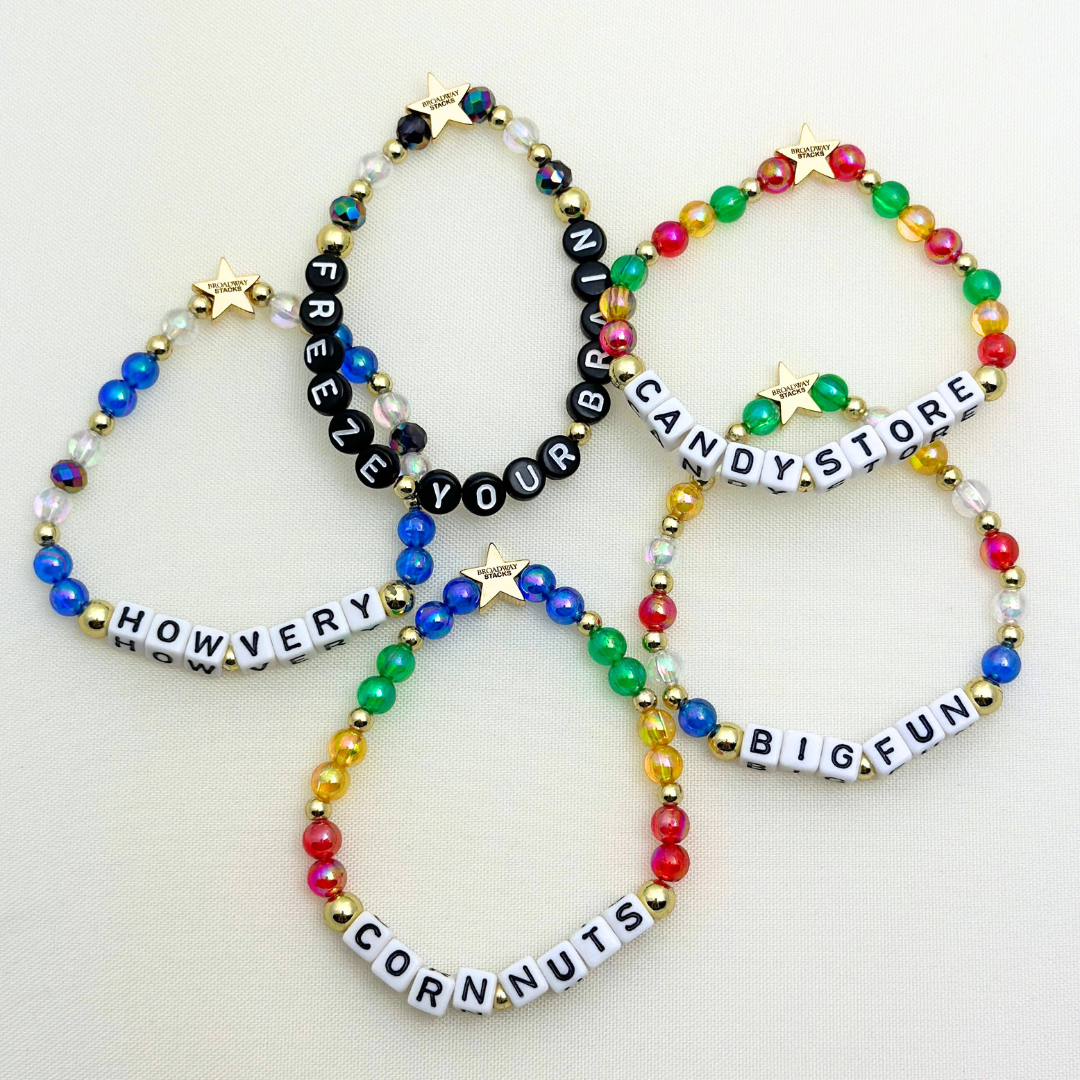 Broadway Stacks CORN NUTS Collection. 5 stretch bracelets included in Stack. Red, yellow, green, blue, black and gold colored beads. Letter beads that spell quotes. Gold star logo bead to remind you that you shine. Heathers the Musical fans.