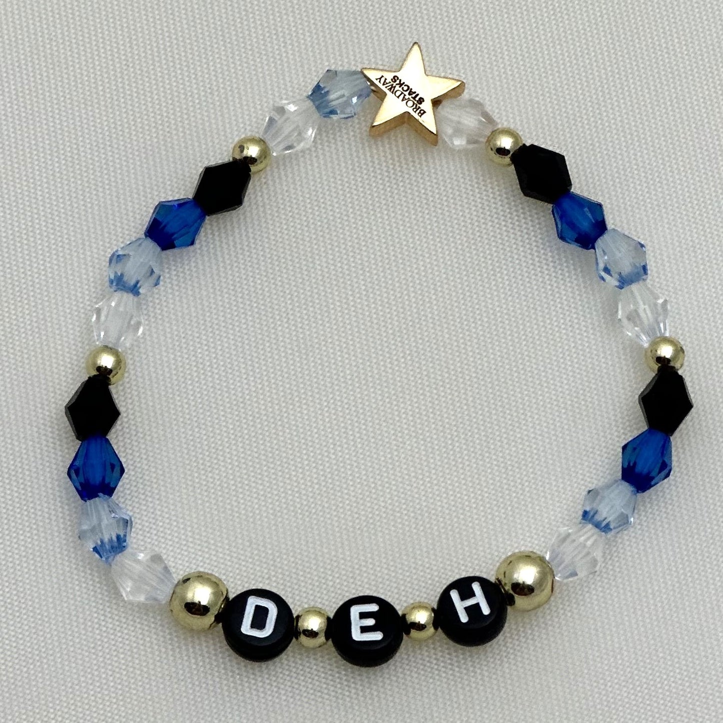 Broadway Stacks SKY collection. 3 stretch bracelets included in Stack. Blues, white, clear, gold and black colored beads. Letter beads that spell show quotes. Broadway Stacks gold star logo bead on back.