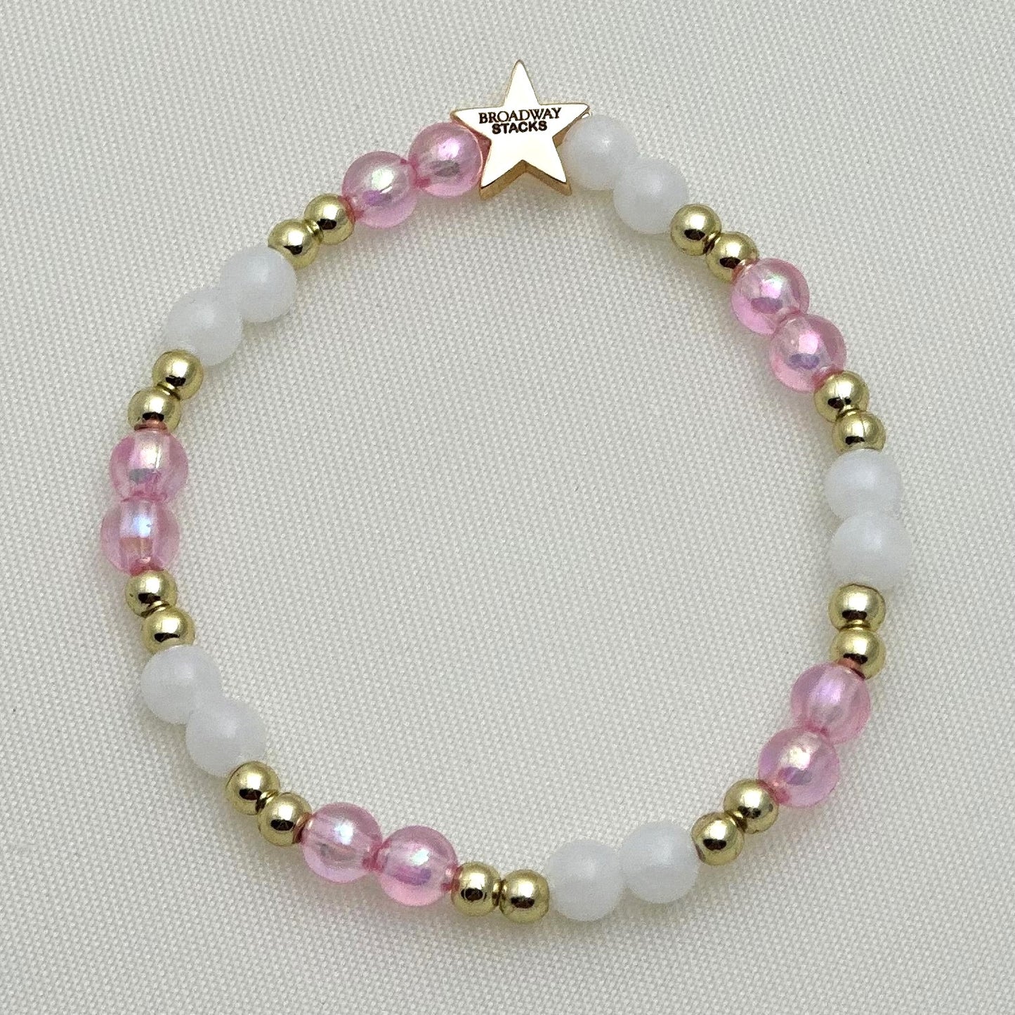 Broadway Stacks KEEP IT POSITIVE collection. 3 stretch bracelets included in Stack. Pinks, white, and gold colored beads. Letter beads that spell show quotes. Broadway Stacks gold star logo bead on back.