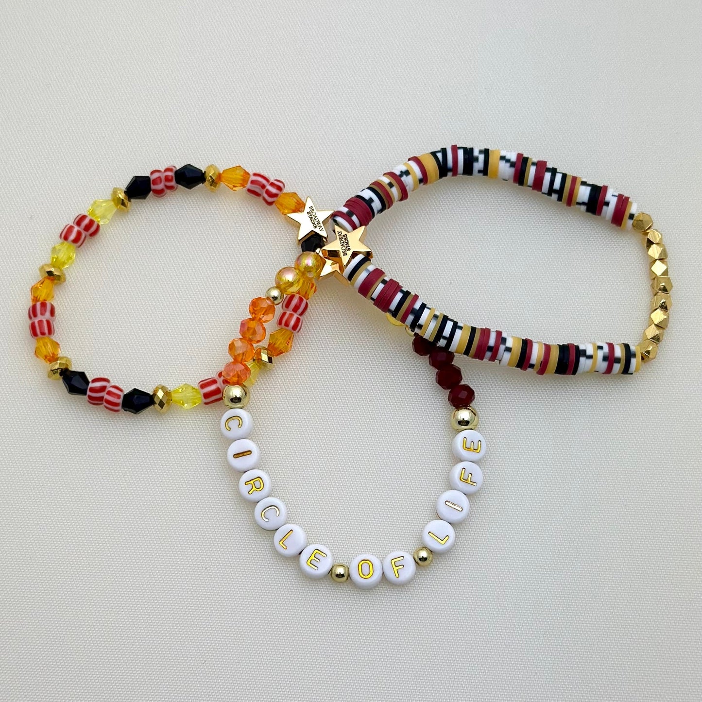 Broadway Stacks SAFARI collection. 3 stretch bracelets included in Stack. Reds, oranges, yellows, black, gold and animal print colored beads. Letter beads that spell show quotes. Broadway Stacks gold star logo bead on back.