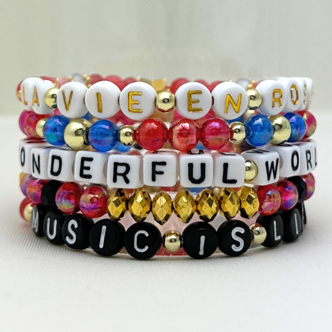 Broadway Stacks JAZZY Collection. 5 stretch bracelets included in Stack. Red, blue, black and gold colored beads. Letter beads that spell quotes. Gold star logo bead to remind you that you shine.