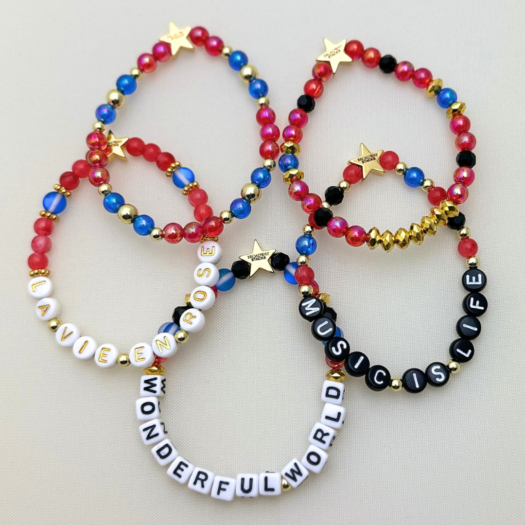 Broadway Stacks JAZZY Collection. 5 stretch bracelets included in Stack. Red, blue, black and gold colored beads. Letter beads that spell quotes. Gold star logo bead to remind you that you shine.