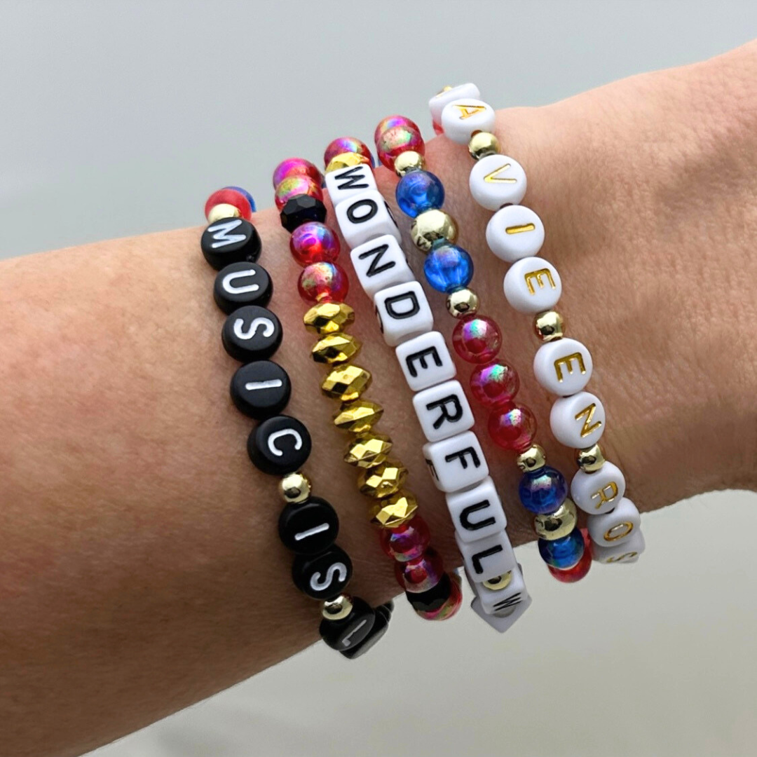 Broadway Stacks JAZZY Collection. 5 stretch bracelets included in Stack. Red, blue, black and gold colored beads. Letter beads that spell quotes. Gold star logo bead to remind you that you shine.