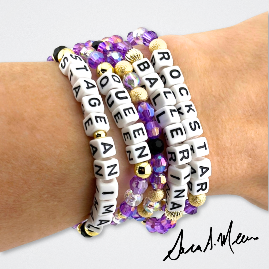 Broadway Stacks Special Edition Sara Mearns ROCKSTAR Bracelet Collection. 5 stretch bracelets included in Stack. Purple, clear, white, black and gold colored beads. Letter beads that spell quotes. Gold star logo bead to remind you that you shine. Sara Mearns and Ballet fans.