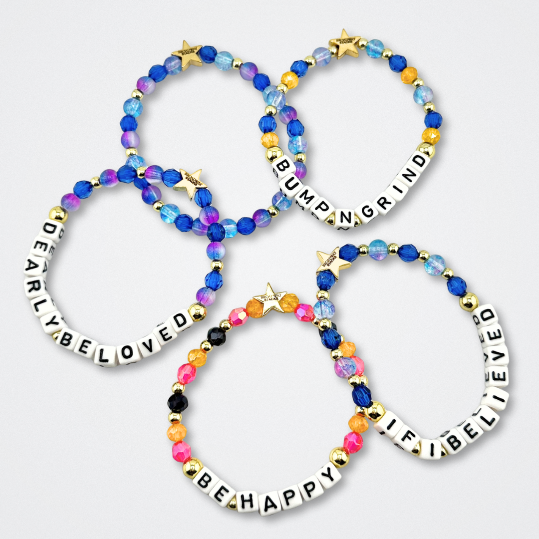 Broadway Stacks CAKE Collection. Five bracelets laying flat with letter beads that spell quotes. Blues, purple, yellow, pink, black and gold colored beads. Two Strangers Carry a Cake Across New York fans.