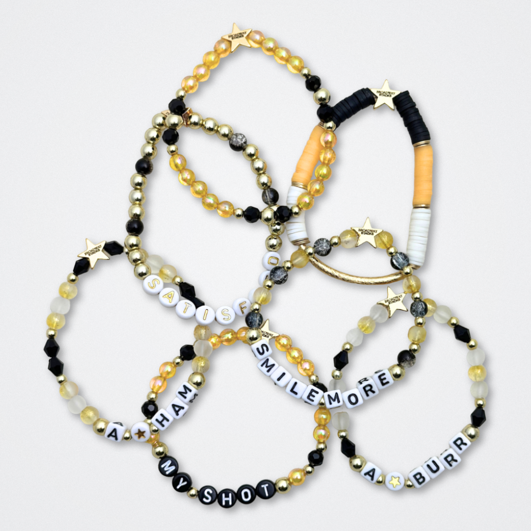 Broadway Stacks REVOLUTION Collection. 5 stretch bracelets included in Stack. Yellow, white, black and gold colored beads. Letter beads that spell quotes. Gold star logo bead to remind you that You Shine. Hamilton the Musical fans.