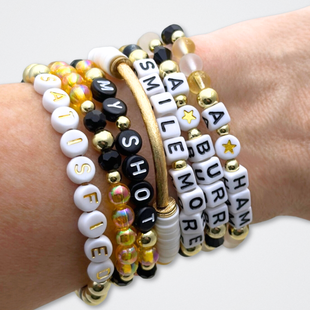 Broadway Stacks REVOLUTION Collection. 5 stretch bracelets included in Stack. Yellow, white, black and gold colored beads. Letter beads that spell quotes. Gold star logo bead to remind you that You Shine. Hamilton the Musical fans.