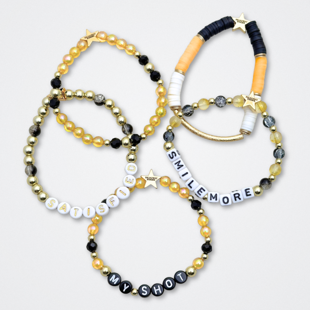 Broadway Stacks REVOLUTION Collection. 5 stretch bracelets included in Stack. Yellow, white, black and gold colored beads. Letter beads that spell quotes. Gold star logo bead to remind you that You Shine. Hamilton the Musical fans.