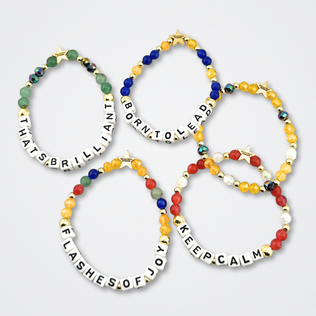 Broadway Stacks CONFIDENTIAL Collection. 5 stretch bracelets laid flat. Black, white, red, blue, green, yellow and gold colored beads. Letter beads that spell quotes. Star logo bead to remind you that you shine. Operation Mincemeat fans.