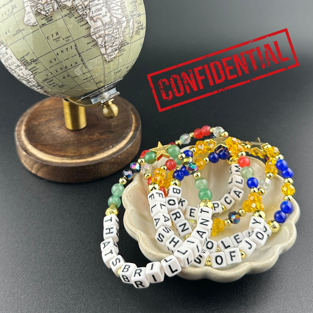 Broadway Stacks CONFIDENTIAL Collection. 5 stretch bracelets in a dish with small globe. Confidential stamped on top. Letter beads that spell quotes. Operation Mincemeat fans.