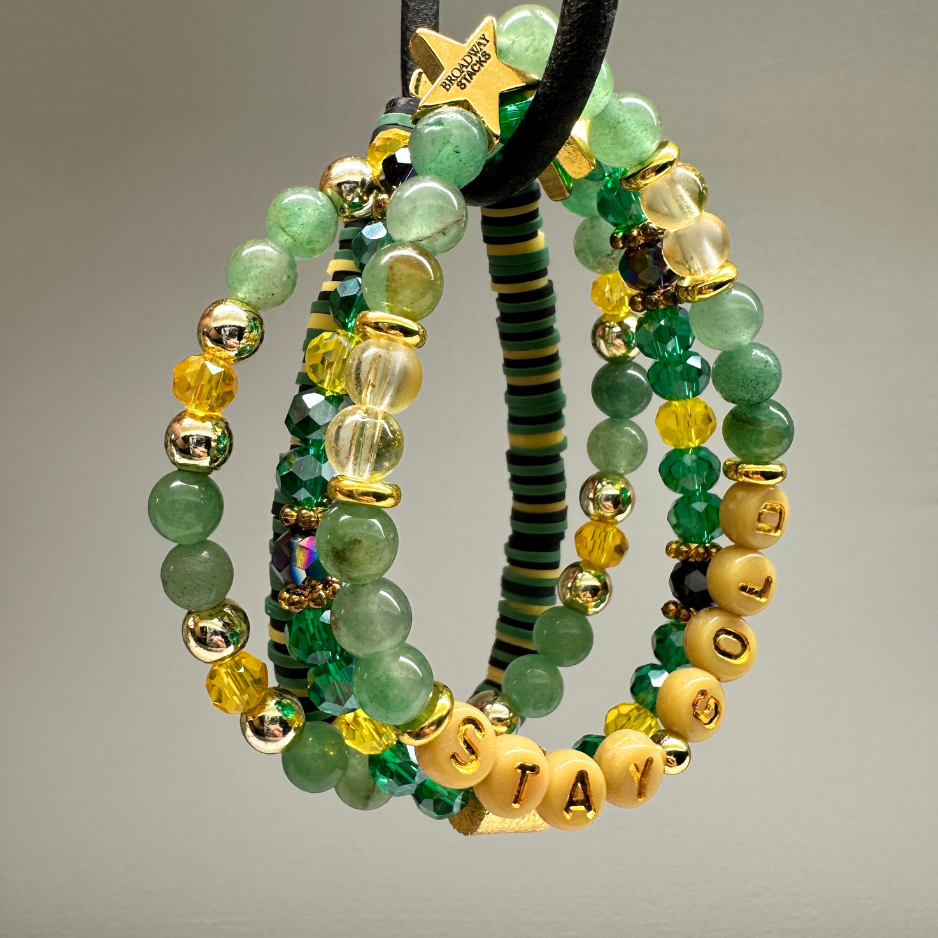 Broadway Stacks STAY GOLD collection. Stretch bracelets included in Stack. Gold, yellow, green and grey colored beads. Letter beads that have show quote or name. Broadway Stacks gold star logo bead to remind you that You Shine. The Outsiders the Musical fans.