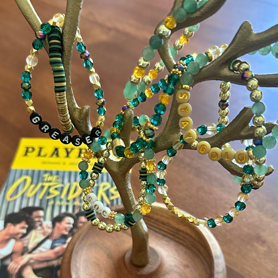 Broadway Stacks STAY GOLD collection. Stretch bracelets included in Stack. Gold, yellow, green and grey colored beads. Letter beads that have show quote or name. Broadway Stacks gold star logo bead to remind you that You Shine. The Outsiders the Musical fans.