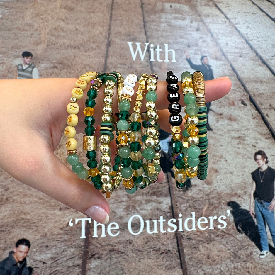 Broadway Stacks STAY GOLD collection. Stretch bracelets included in Stack. Gold, yellow, green and grey colored beads. Letter beads that have show quote or name. Broadway Stacks gold star logo bead to remind you that You Shine. The Outsiders the Musical fans.