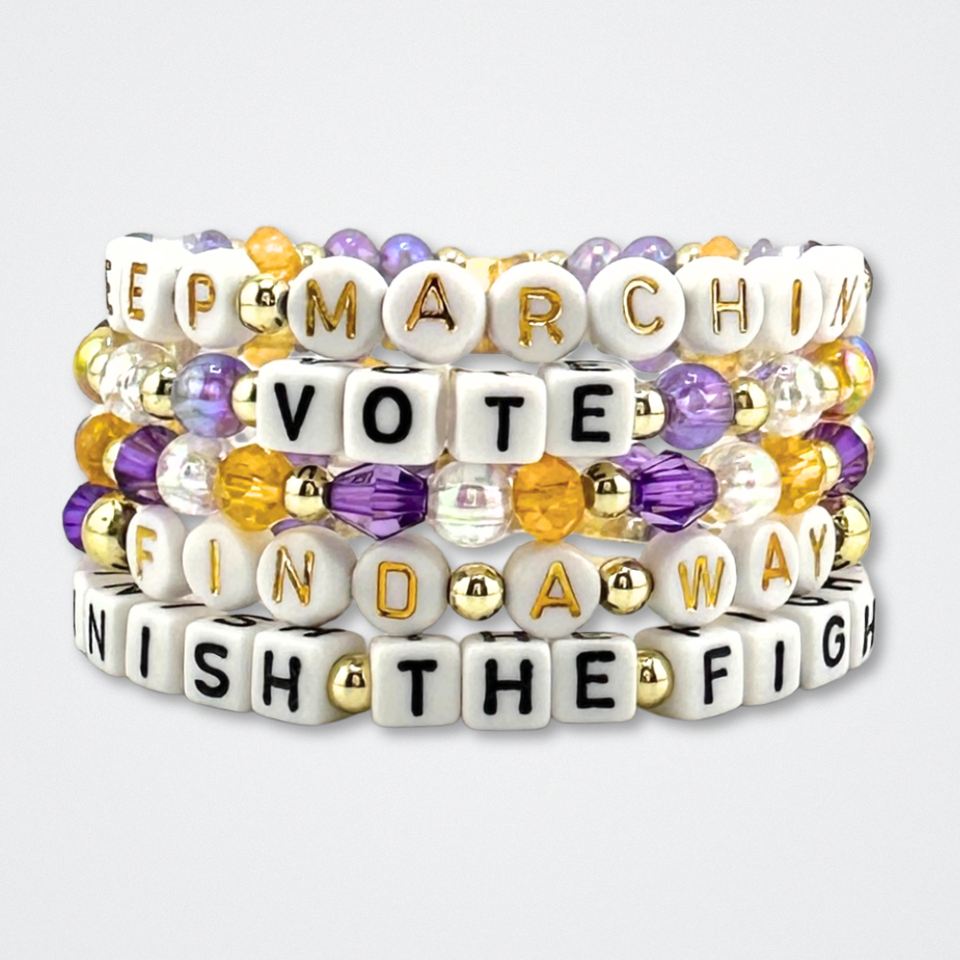 Broadway Stacks CAMPAIGN Collection. Purple, yellow, clear and gold colored bead bracelets stacked on a gray background. Inspired by Suffs the Musical.