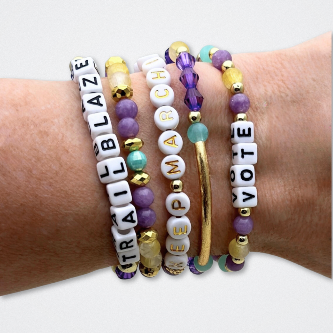 Broadway Stacks CAMPAIGN Collection. 5 stretch bracelets included in Stack. Purple, yellow, teal and gold colored beads. Letter beads that spell quotes. Gold star logo bead to remind you that you shine. Suffs fans.