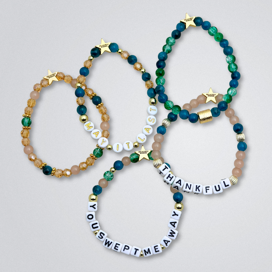 Broadway Stacks SAILOR Collection. 5 stretch bracelets included in Stack. Teal, green, blue and gold colored beads. Letter beads that spell quotes. Swept Away the Musical. Gold star logo bead to remind you that you shine.