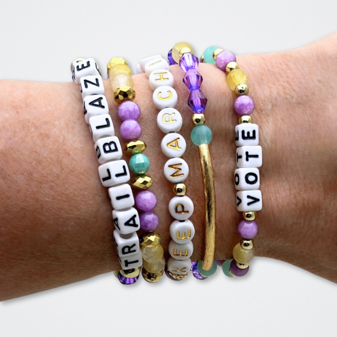 Broadway Stacks CAMPAIGN Collection. 5 stretch bracelets included in Stack. Purple, yellow, teal and gold colored beads. Letter beads that spell quotes. Gold star logo bead to remind you that you shine. Suffs fans.