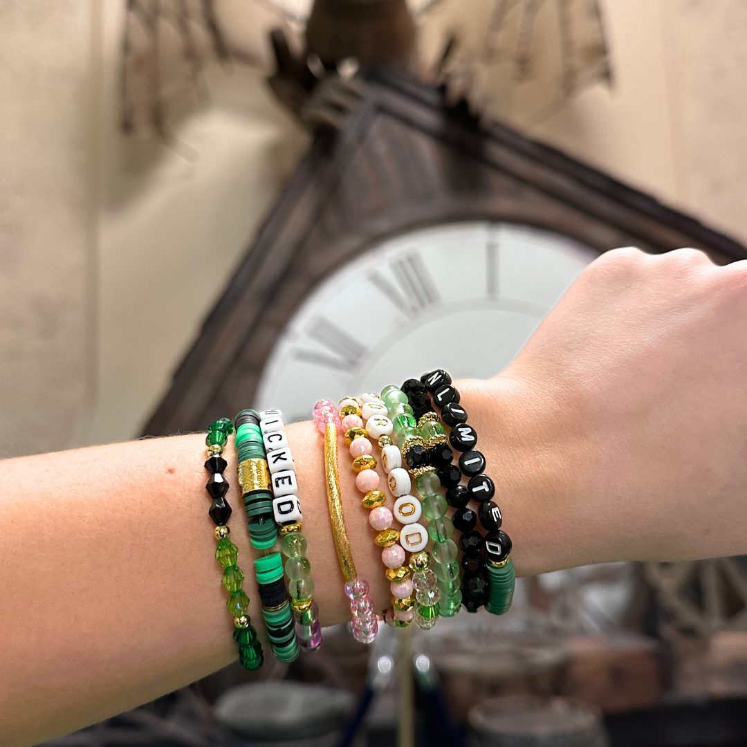 Broadway Stacks Witch collection. 3 stretch bracelets included in Stack. Greens, pinks, black and gold colored beads. Letter beads that spell Wicked. Gold star logo bead on every bracelet.