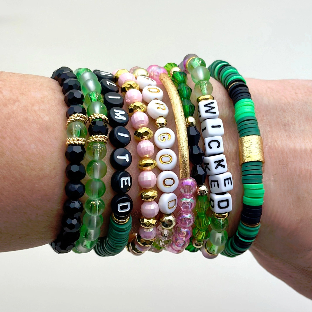 Broadway Stacks Witch collection. 3 stretch bracelets included in Stack. Greens, pinks, black and gold colored beads. Letter beads that spell Wicked. Gold star logo bead on every bracelet.