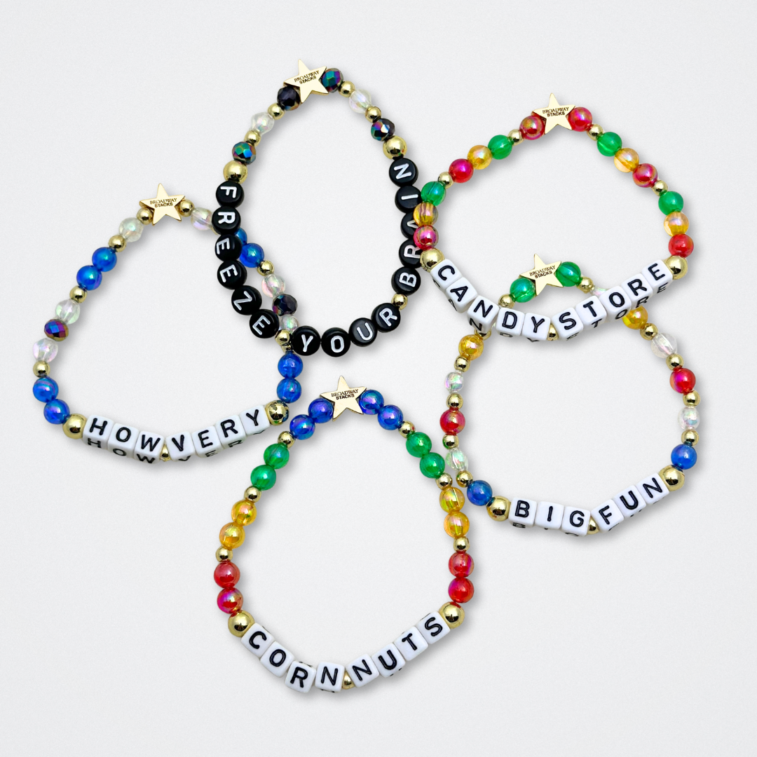 Broadway Stacks CORN NUTS Collection. 5 stretch bracelets included in Stack. Red, yellow, green, blue, black and gold colored beads. Letter beads that spell quotes. Gold star logo bead to remind you that you shine. Heathers the Musical fans.