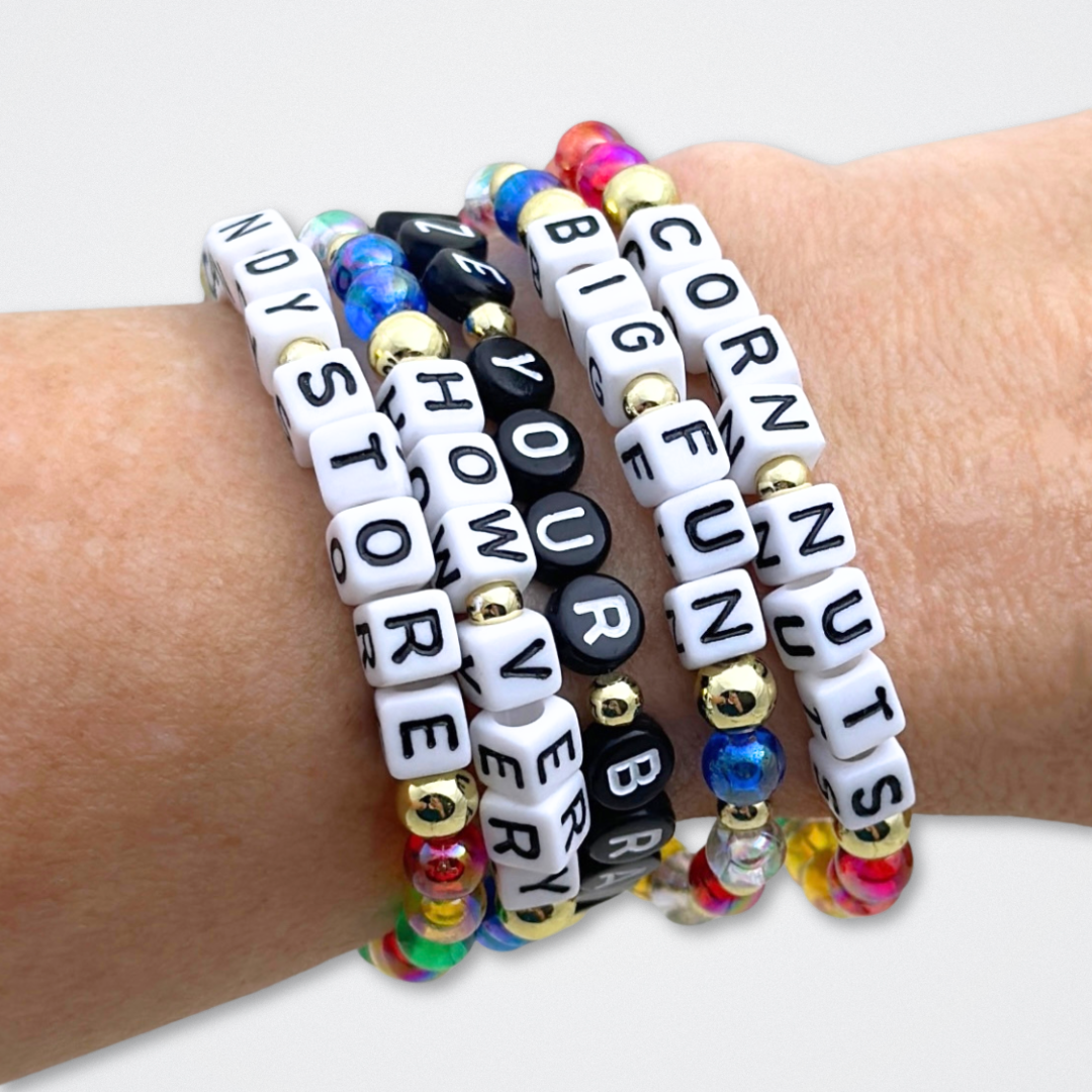 Broadway Stacks CORN NUTS Collection. 5 stretch bracelets included in Stack. Red, yellow, green, blue, black and gold colored beads. Letter beads that spell quotes. Gold star logo bead to remind you that you shine. Heathers the Musical fans.