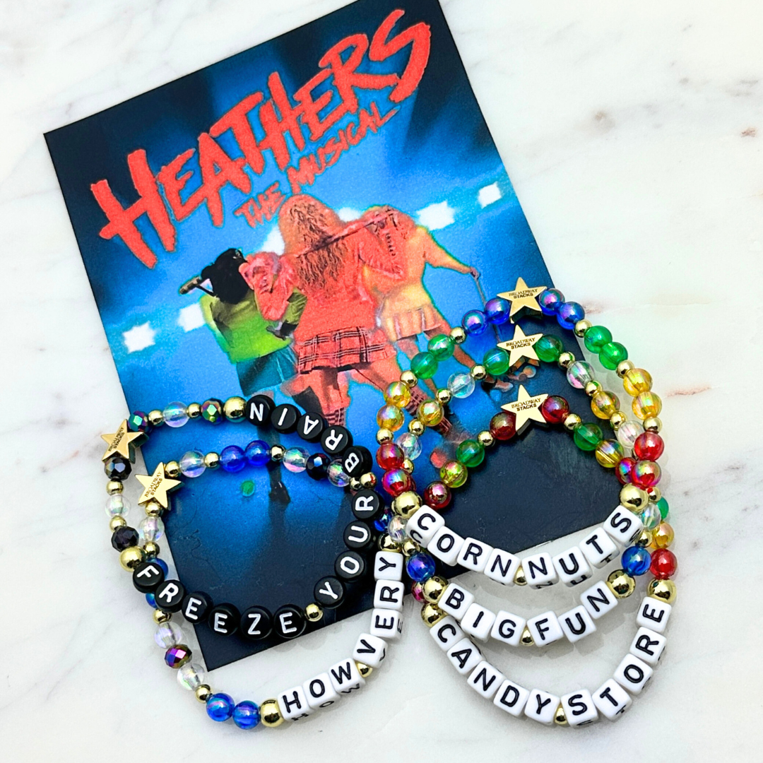 Broadway Stacks CORN NUTS Collection. 5 stretch bracelets included in Stack. Red, yellow, green, blue, black and gold colored beads. Letter beads that spell quotes. Gold star logo bead to remind you that you shine. Heathers the Musical fans.