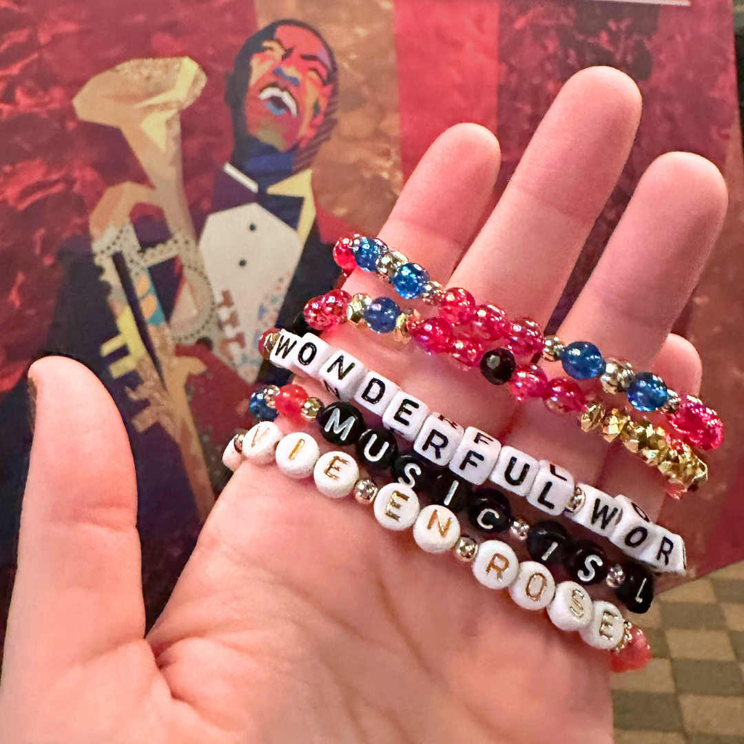 Broadway Stacks JAZZY Collection. 5 stretch bracelets included in Stack. Red, blue, black and gold colored beads. Letter beads that spell quotes. Gold star logo bead to remind you that you shine. Wonderful World musical and Louis Armstrong fans.