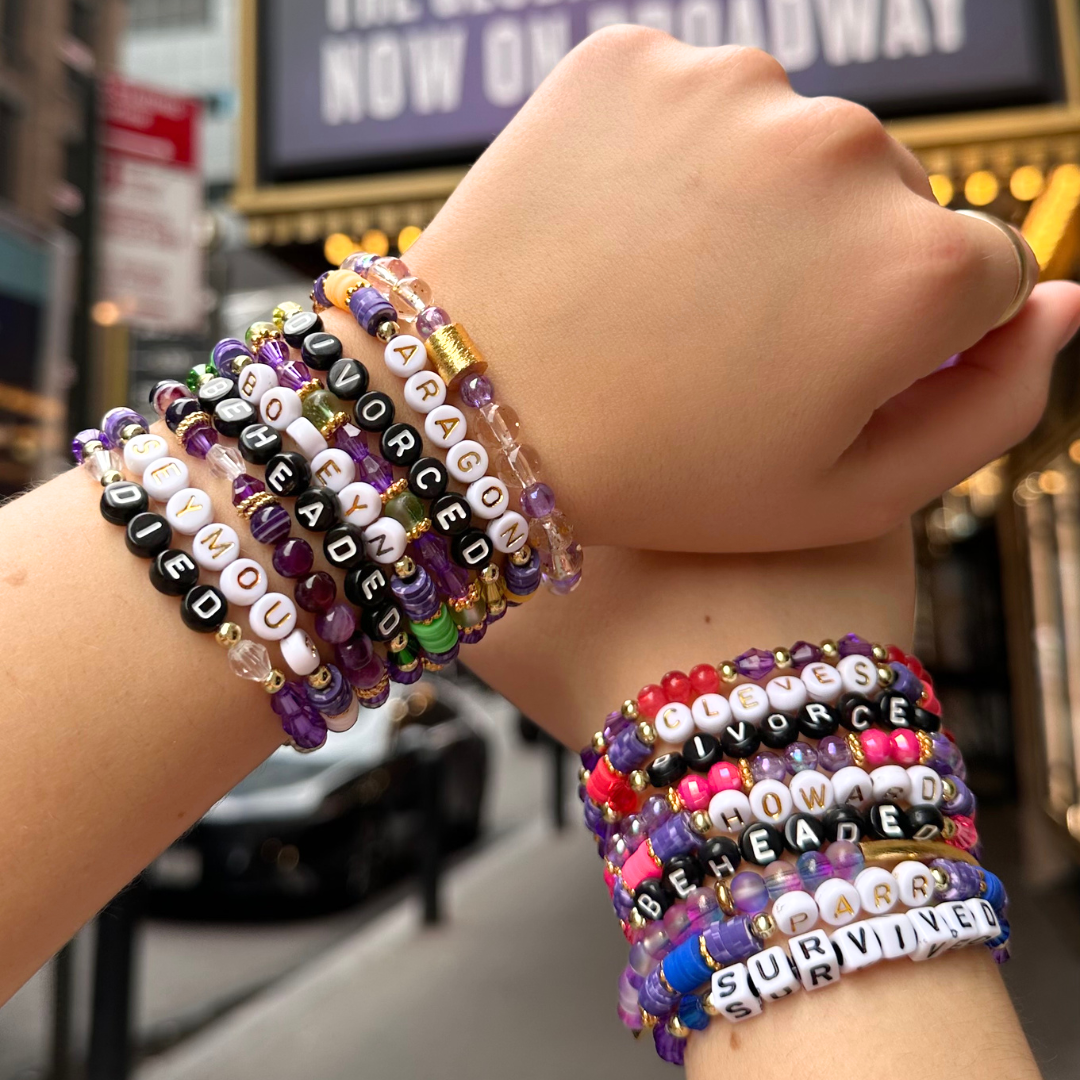 Broadway Stacks QUEEN bracelets. Gold, yellow, green, white, red, pink and blue colored beads. Letter beads that spell each queen. Also Herstory collection. Broadway Stacks gold star logo bead to remind you that You Shine. SIX the Musical fans.