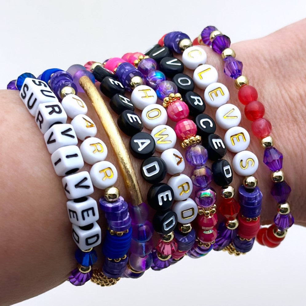 Broadway Stacks QUEEN collection. Stretch bracelets included in Stack. Gold, yellow, green, white, red, pink and blue colored beads. Letter beads that spell each queen. Also Herstory collection. Broadway Stacks gold star logo bead on back.