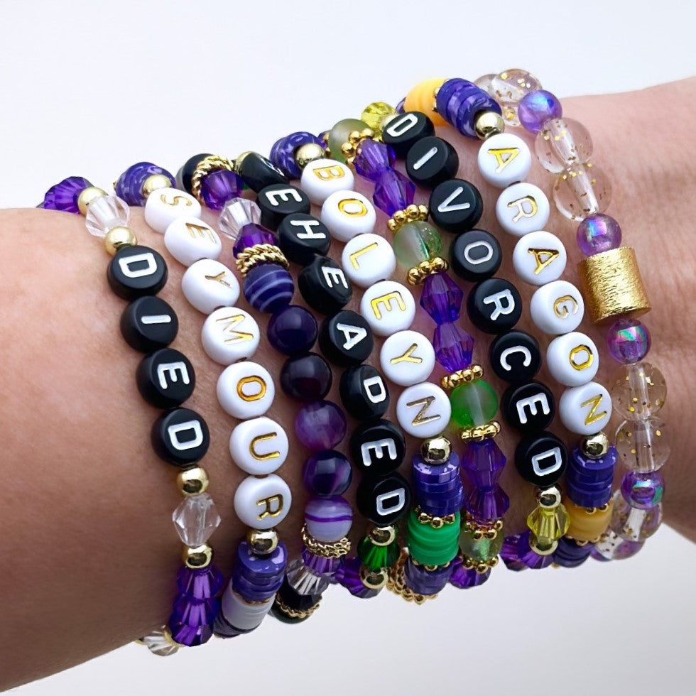 Broadway Stacks QUEEN collection. Stretch bracelets included in Stack. Gold, yellow, green, white, red, pink and blue colored beads. Letter beads that spell each queen. Also Herstory collection. Broadway Stacks gold star logo bead on back.