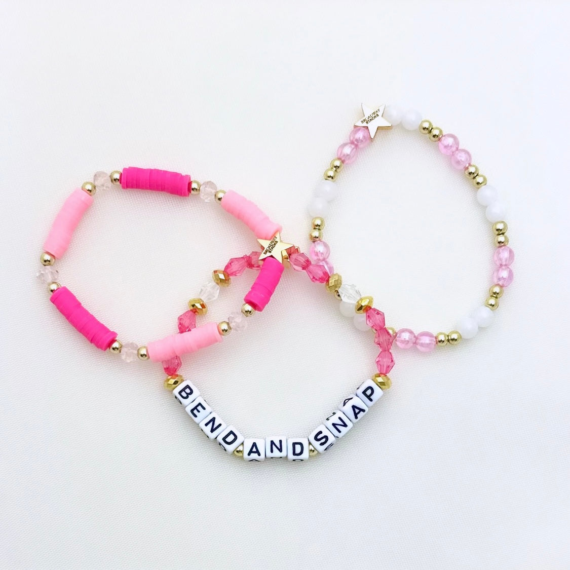 Broadway Stacks Bend and Snap collection. 3 stretch bracelets included in Stack. Pinks, white and gold colored beads. Letter beads that spell Bend and Snap.