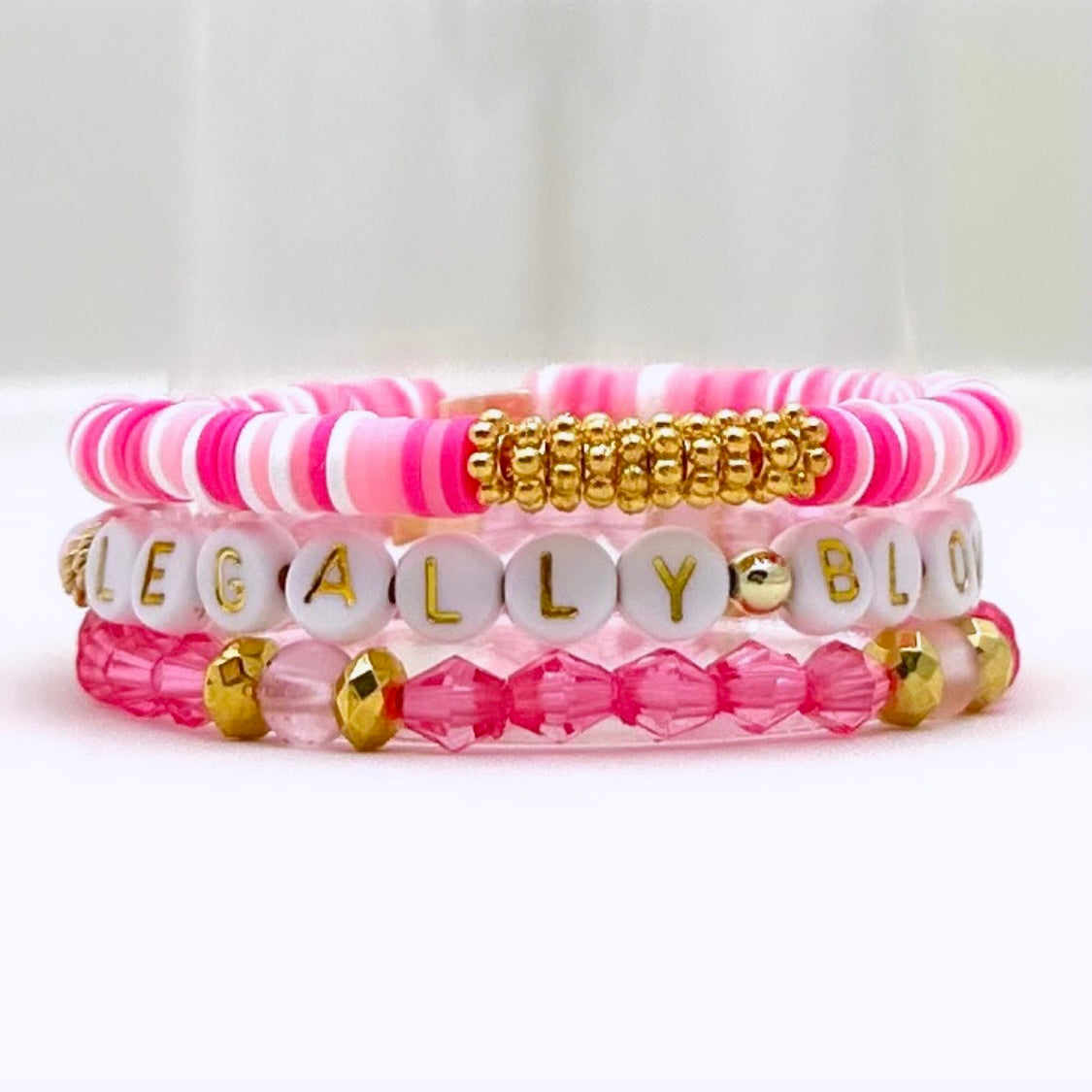 Broadway Stacks KEEP IT POSITIVE collection. 3 stretch bracelets included in Stack. Pinks, white, and gold colored beads. Letter beads that spell show quotes. Broadway Stacks gold star logo bead on back.