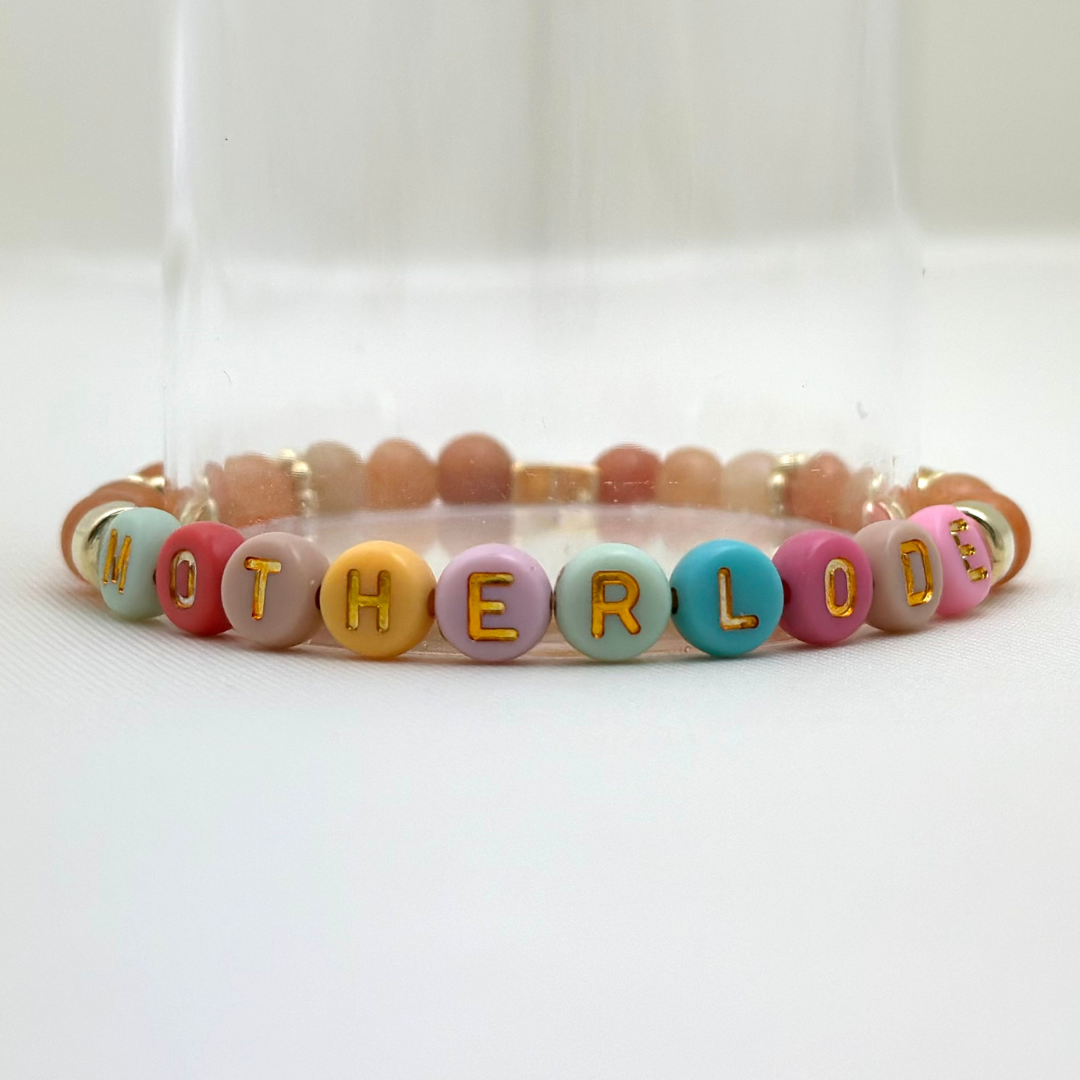 Broadway Stacks Motherlode Special Edition bracelets. Stretch bracelets. Greens, browns, white and gold colored beads. Letter beads that spell Motherlode, Boy Mom, Girl Mom, Twin Mom,