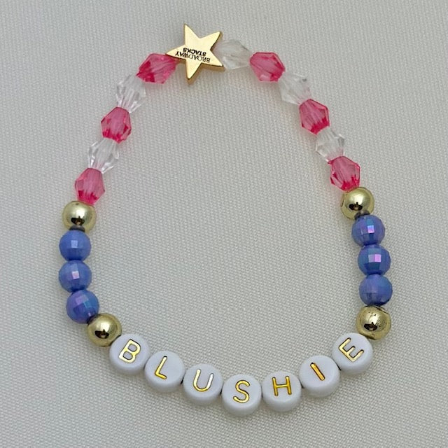 Broadway Stacks POTUS collection. 3 stretch bracelets included in Stack. Pinks, white, blue, golds and black colored beads. Letter beads that spell show quotes. Broadway Stacks gold star logo bead on back.