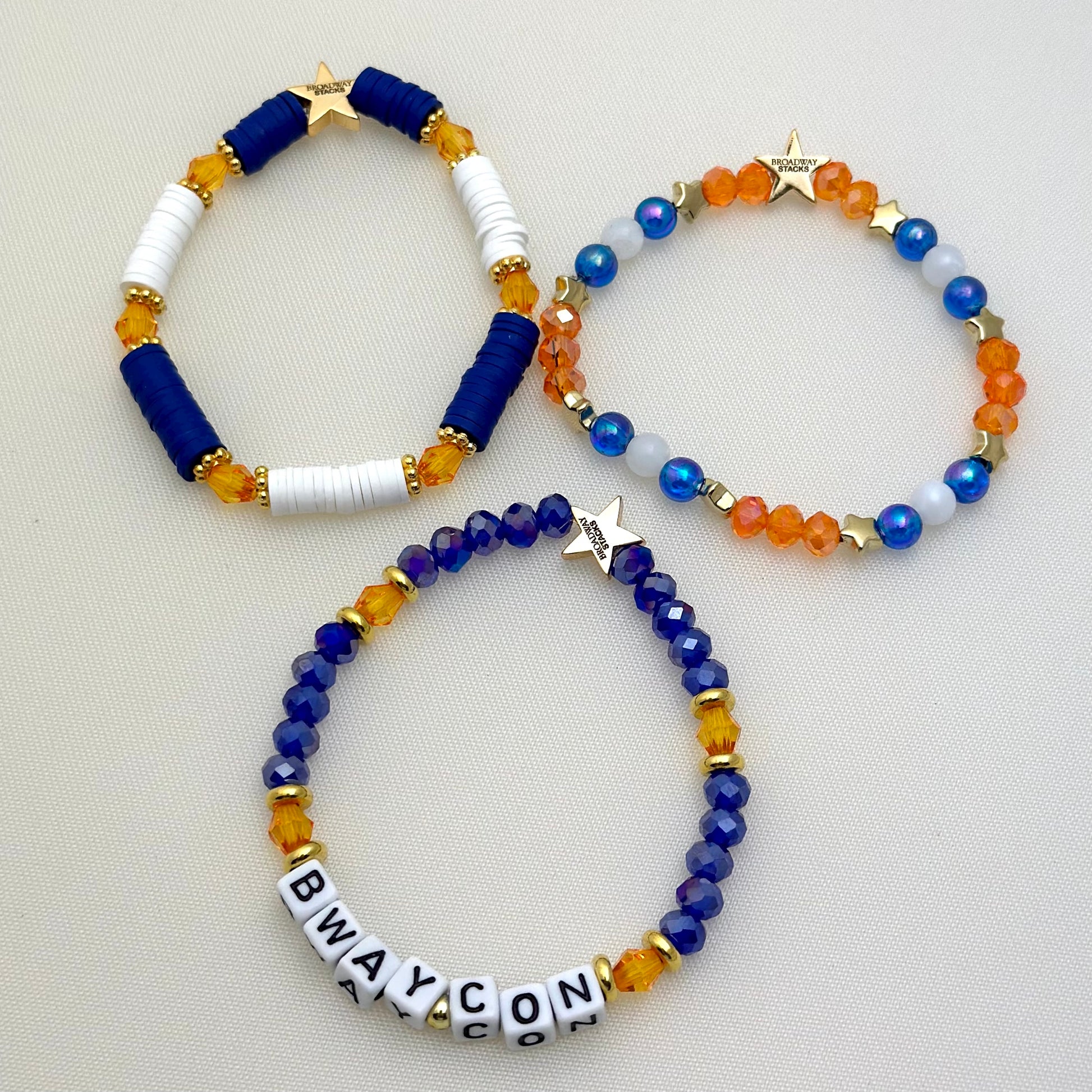 Broadway Stacks BroadwayCon 2024 Stack bracelets. 3 stretch bracelets. Blue, orange, white and gold colored beads. Letter beads that spell Bway Con. All have star logo bead.