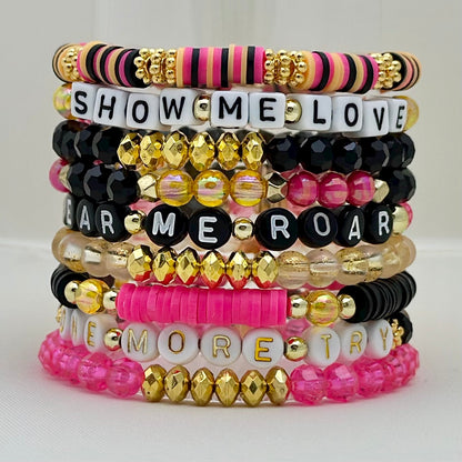 Broadway Stacks De Bois Band collection. 3 stretch bracelets included in Stack. Pinks, golds and black colored beads. Letter beads that spell One More Try. Broadway Stacks gold star logo bead on back.