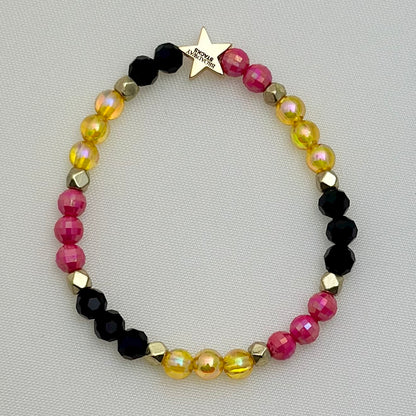 Broadway Stacks De Bois Band collection. 3 stretch bracelets included in Stack. Pinks, golds and black colored beads. Letter beads that spell Hear Me Roar. Broadway Stacks gold star logo bead on back.