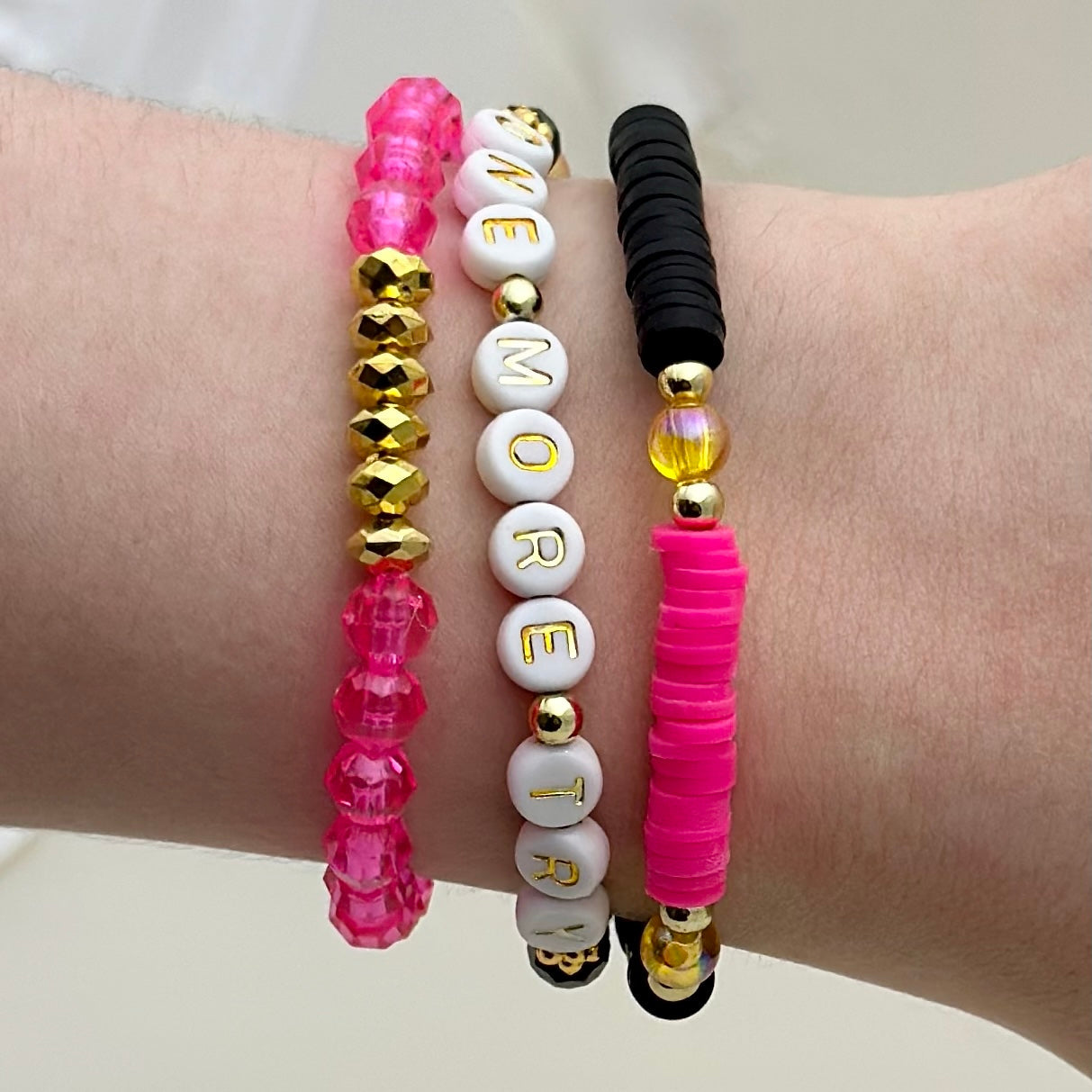 Broadway Stacks De Bois Band collection. 3 stretch bracelets included in Stack. Pinks, golds and black colored beads. Letter beads that spell One More Try. Broadway Stacks gold star logo bead on back.