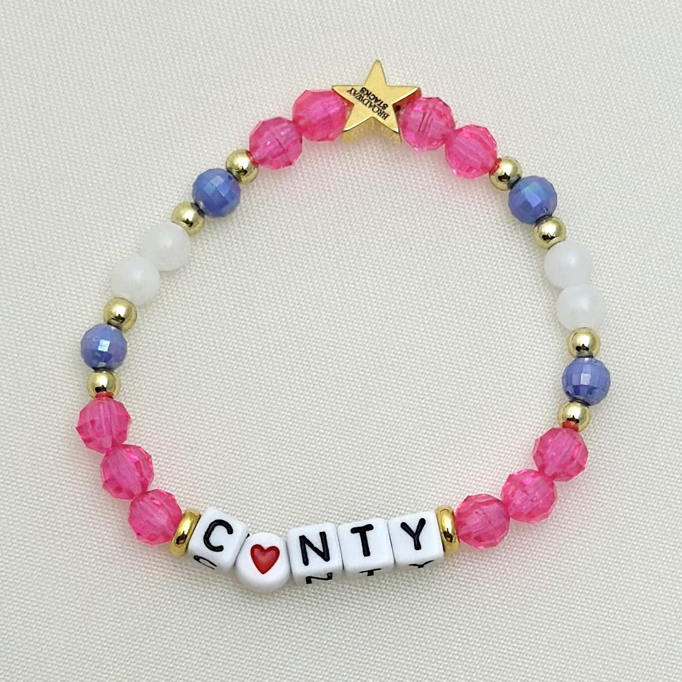 Broadway Stacks POTUS collection. 3 stretch bracelets included in Stack. Pinks, white, blue, golds and black colored beads. Letter beads that spell show quotes. Broadway Stacks gold star logo bead on back.