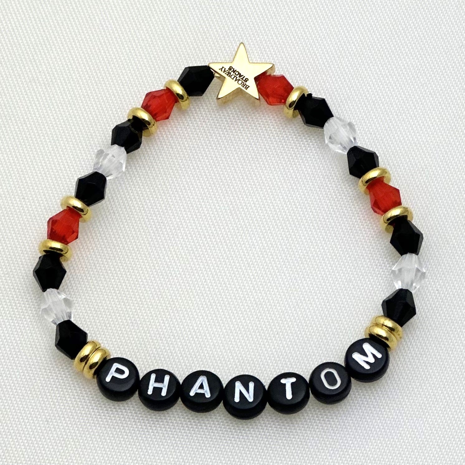 Broadway Stacks MASK collection. 3 stretch bracelets included in Stack. Red, white, gold and black colored beads. Letter beads that spell show quotes. Broadway Stacks gold star logo bead on back.