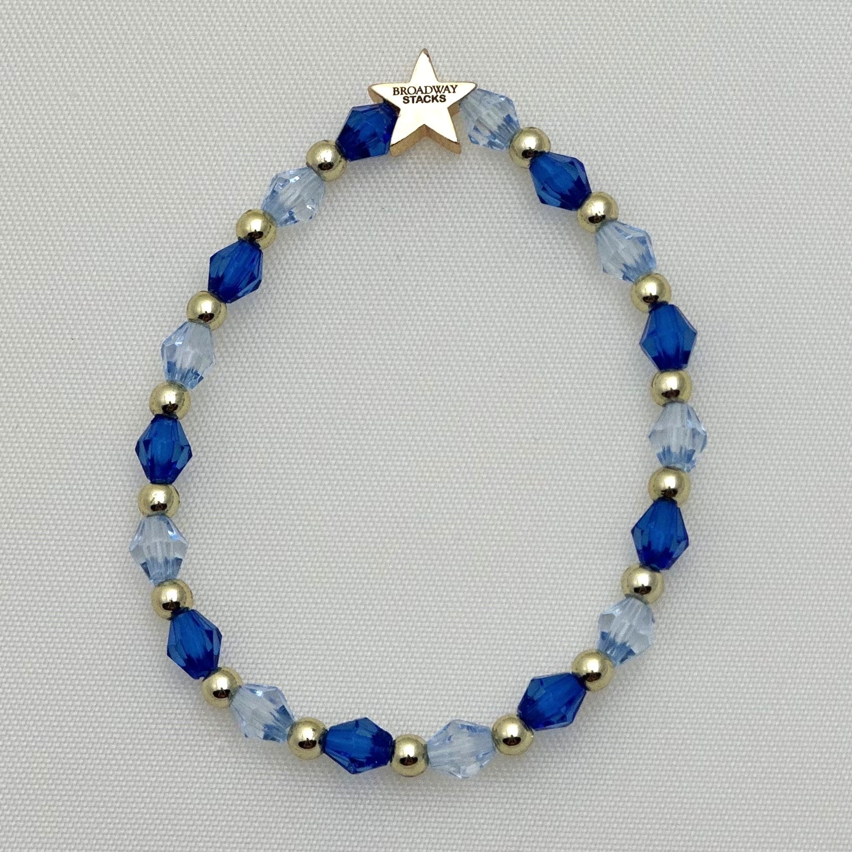 Broadway Stacks SKY collection. 3 stretch bracelets included in Stack. Blues, white, clear, gold and black colored beads. Letter beads that spell show quotes. Broadway Stacks gold star logo bead on back.