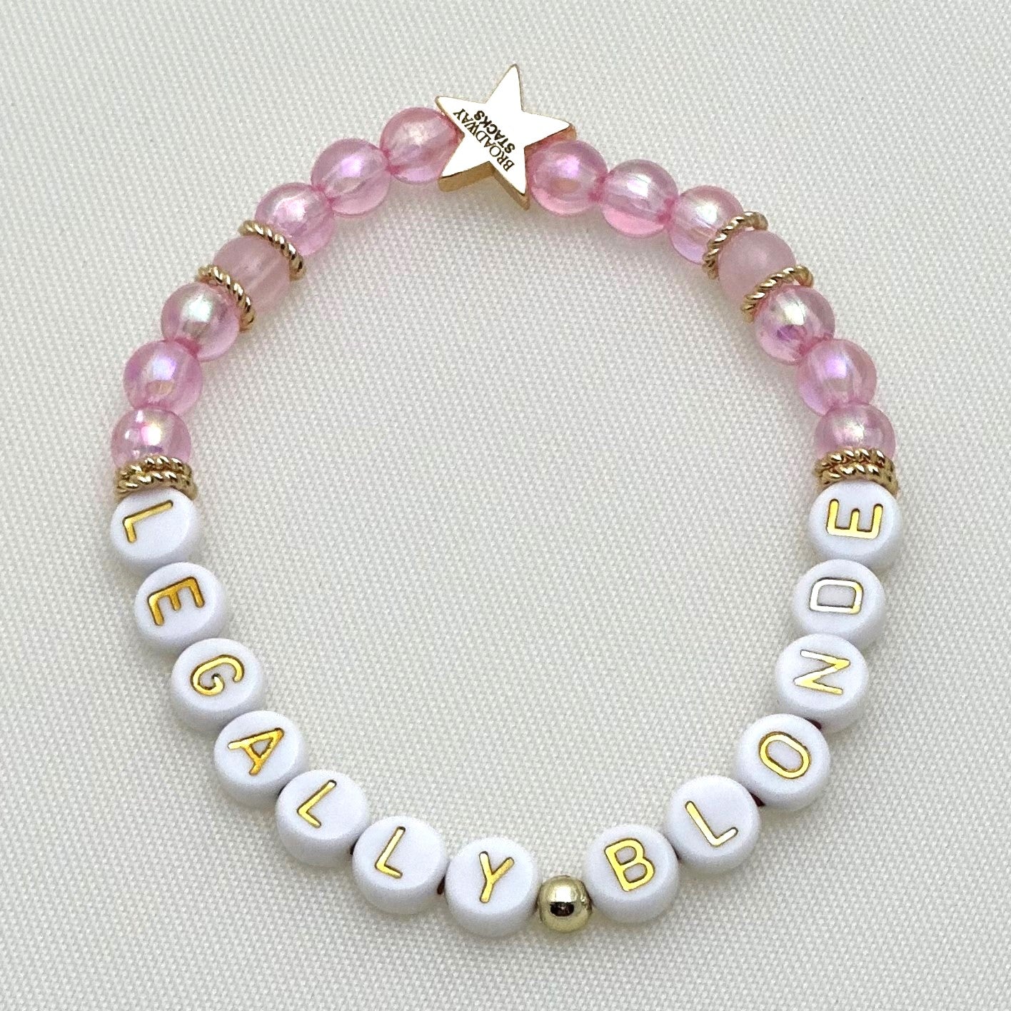 Broadway Stacks KEEP IT POSITIVE collection. 3 stretch bracelets included in Stack. Pinks, white, and gold colored beads. Letter beads that spell show quotes. Broadway Stacks gold star logo bead on back.