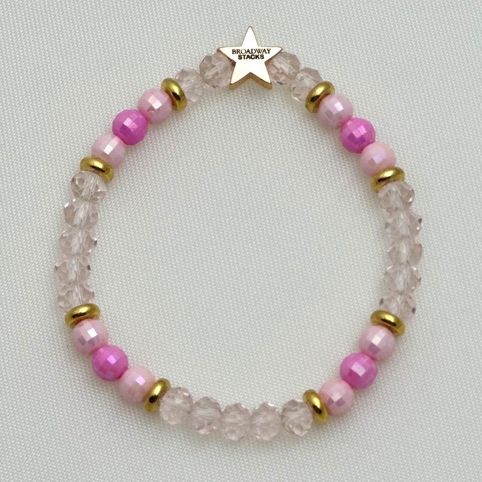 Broadway Stacks KEEP IT POSITIVE collection. 3 stretch bracelets included in Stack. Pinks, white, and gold colored beads. Letter beads that spell show quotes. Broadway Stacks gold star logo bead on back.