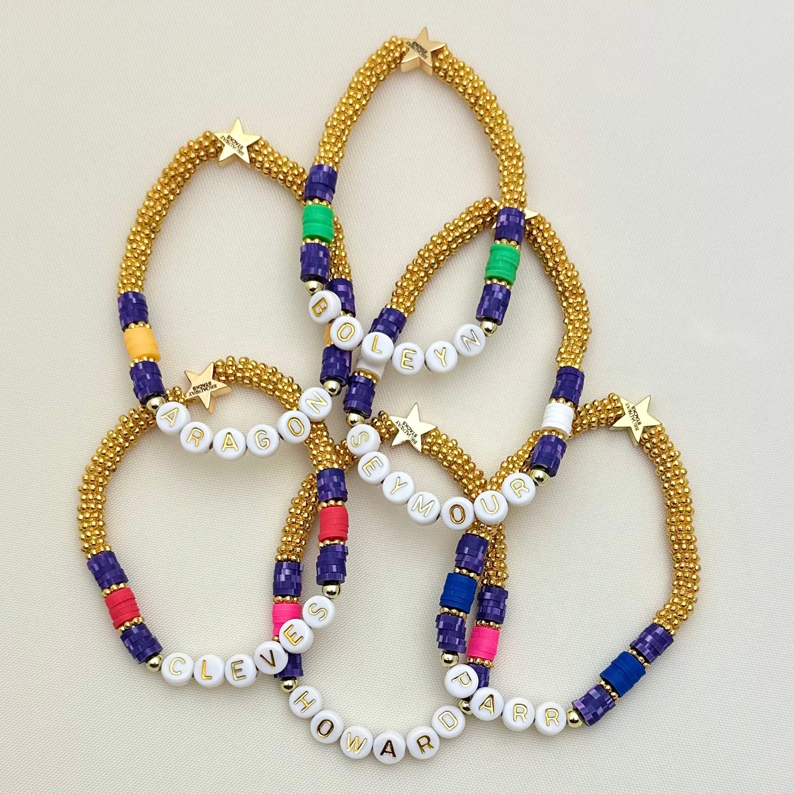 Broadway Stacks QUEEN collection. Stretch bracelets included in Stack. Gold, yellow, green, white, red, pink and blue colored beads. Letter beads that spell each queen. Also Herstory collection. Broadway Stacks gold star logo bead on back.