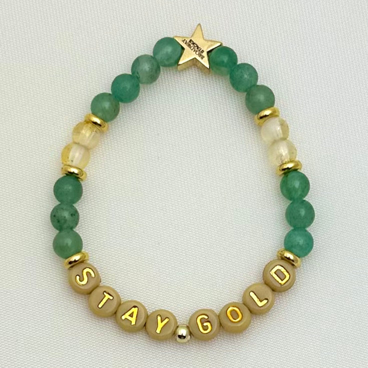 Broadway Stacks STAY GOLD collection. Stretch bracelets included in Stack. Gold, yellow, green and grey colored beads. Letter beads that have show quote or name. Broadway Stacks gold star logo bead on back.