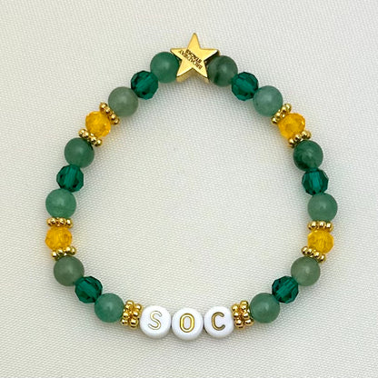 Broadway Stacks STAY GOLD collection. Stretch bracelets included in Stack. Gold, yellow, green and grey colored beads. Letter beads that have show quote or name. Broadway Stacks gold star logo bead on back.