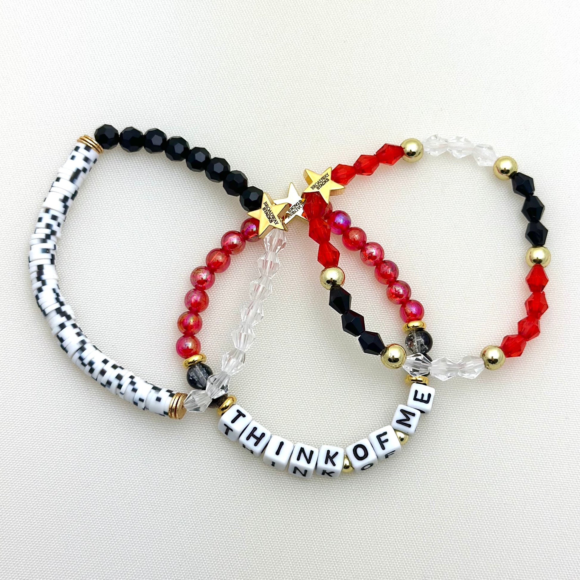 Broadway Stacks MASK collection. 3 stretch bracelets included in Stack. Red, white, gold and black colored beads. Letter beads that spell show quotes. Broadway Stacks gold star logo bead on back.