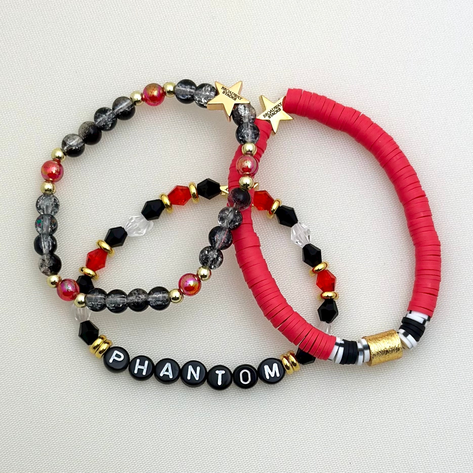 Broadway Stacks Phantom collection. 3 stretch bracelets included in Stack. Red, black, white and gold colored beads. Letter beads that spell Phantom.