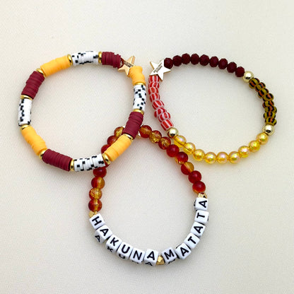 Broadway Stacks SAFARI collection. 3 stretch bracelets included in Stack. Dark reds, yellow, orange, white, black and gold colored beads. Animal print beads as well. Letter beads that spell Hakuna Matata.